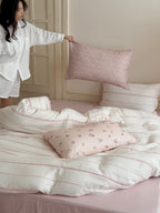 Person arranging pink pillows on a bed with white bedding