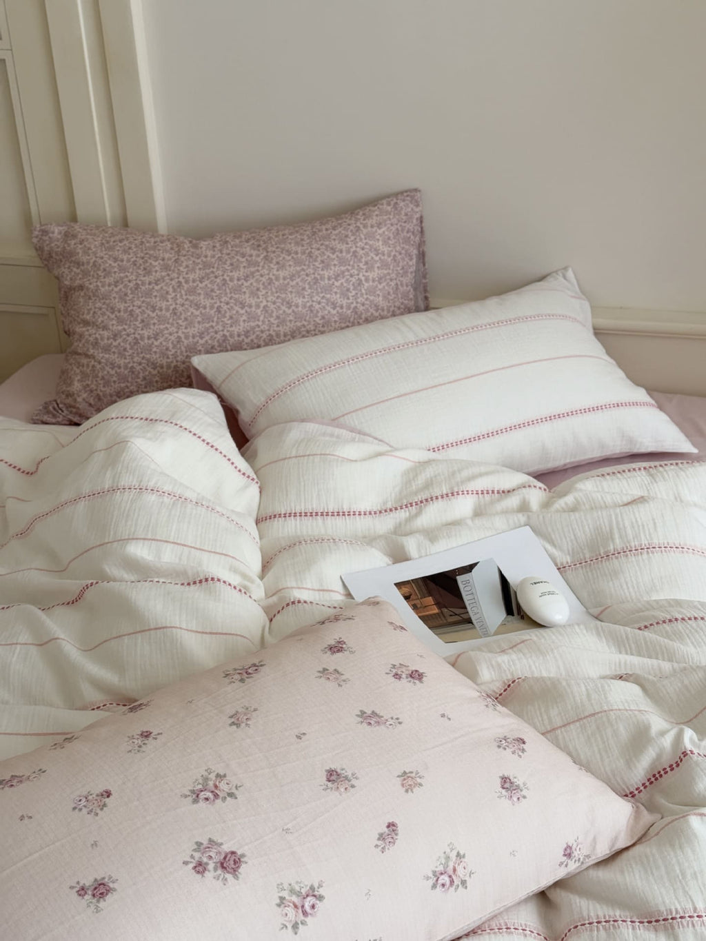 Bed with floral and striped bedding and pillows against a neutral wall.