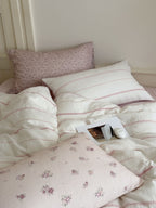 Bed with floral and striped bedding and pillows against a neutral wall.