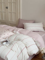 Pink and white bedding set with pillows on a bed in a bedroom.