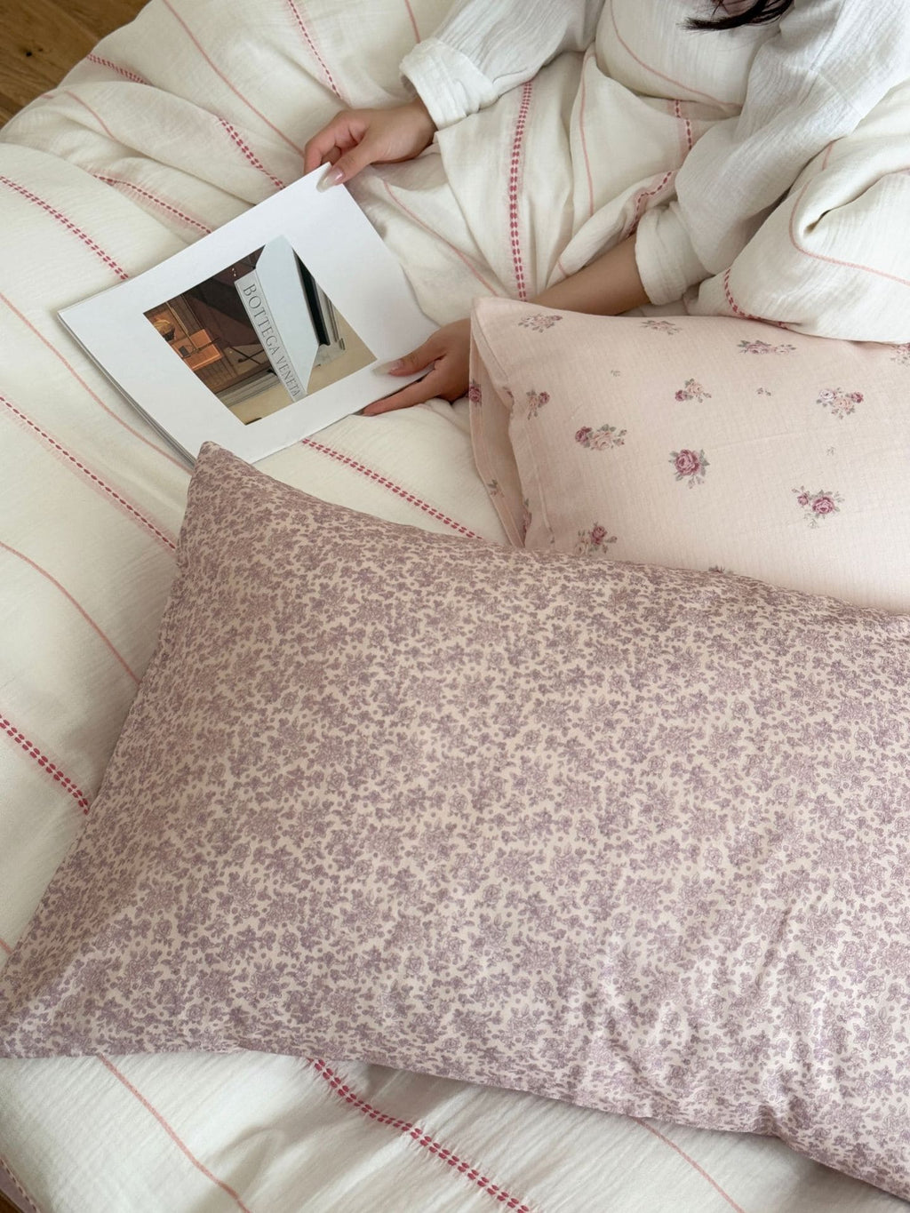 Person reading a book on a floral-patterned bed with a pillow.