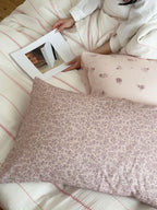 Person reading a book on a floral-patterned bed with a pillow.