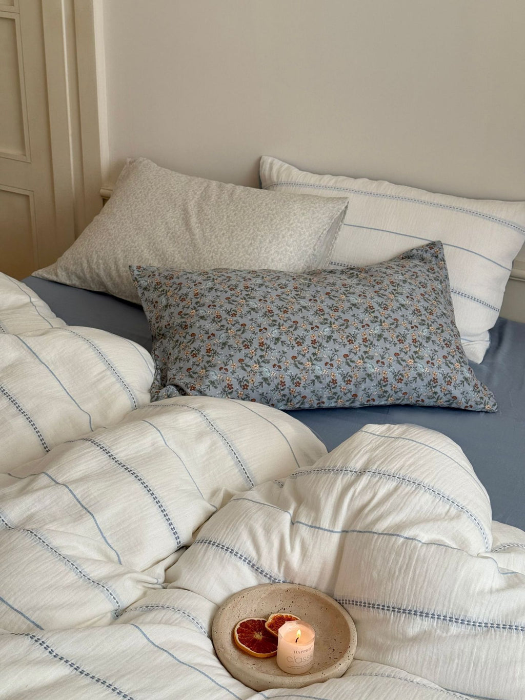Bed with floral and striped pillows and a candle on a wooden coaster.