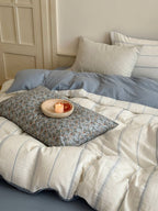 Bed with blue and white bedding, pillows, and a candle on a small table.