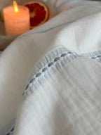 Close-up of a light blue fabric with decorative stitching, a lit candle, and a sliced grapefruit in the background.
