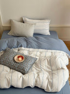 Bed with blue sheets, white and gray pillows, and a blanket with a small plate of fruit on a floral pillow.