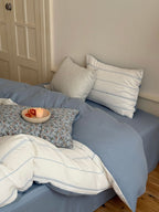 Bed with blue bedding and pillows in a room with a door and wall.