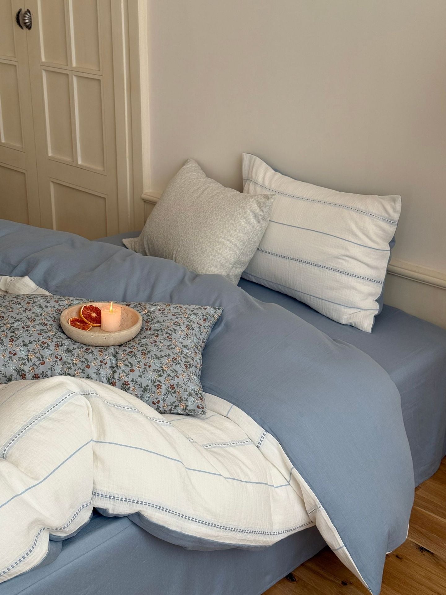 Bed with blue bedding and pillows in a room with a door and wall.