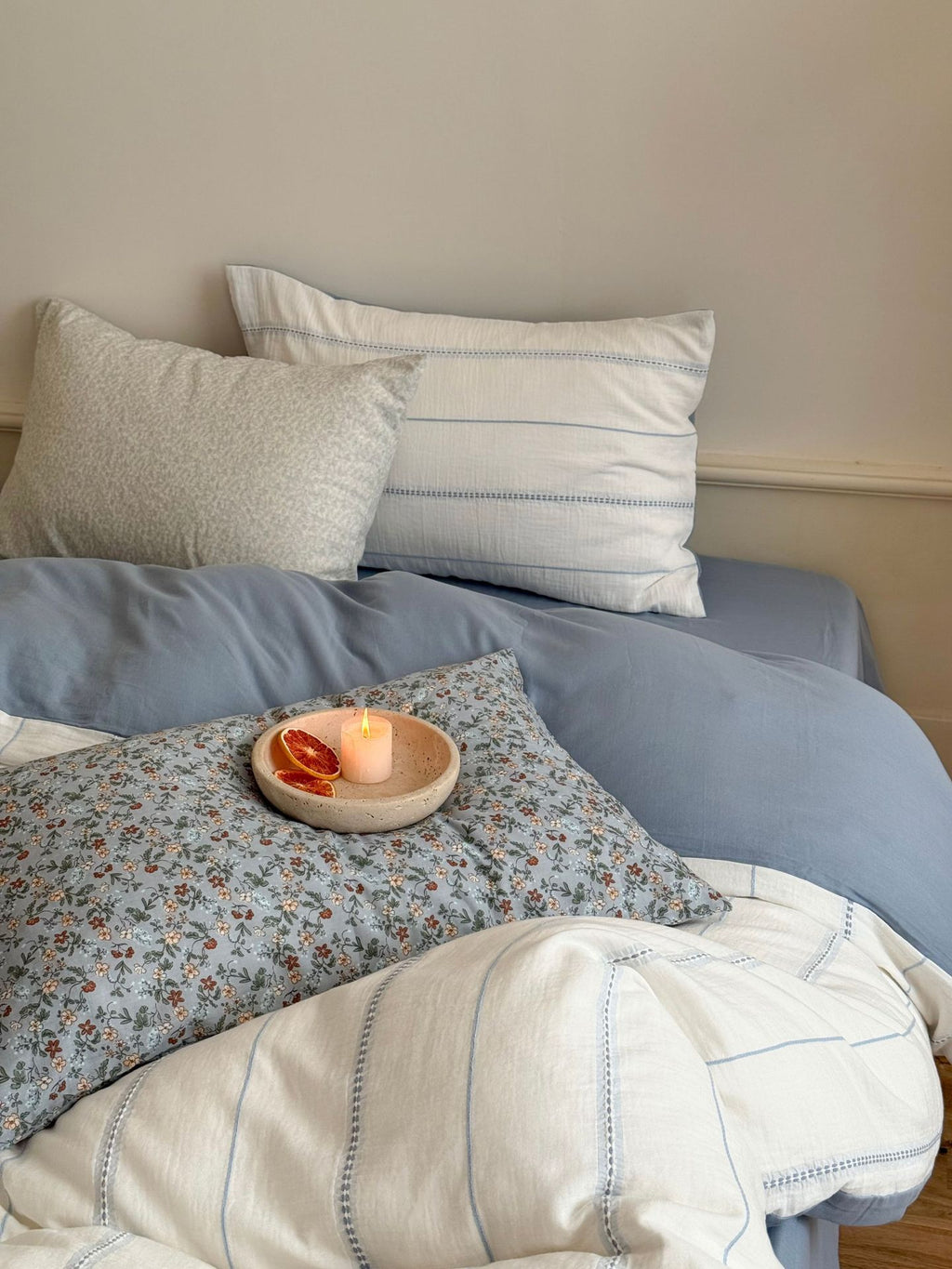 Bed with floral and striped pillows and a candle on a wooden surface.