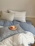 Bed with floral and striped pillows and a candle on a wooden surface.