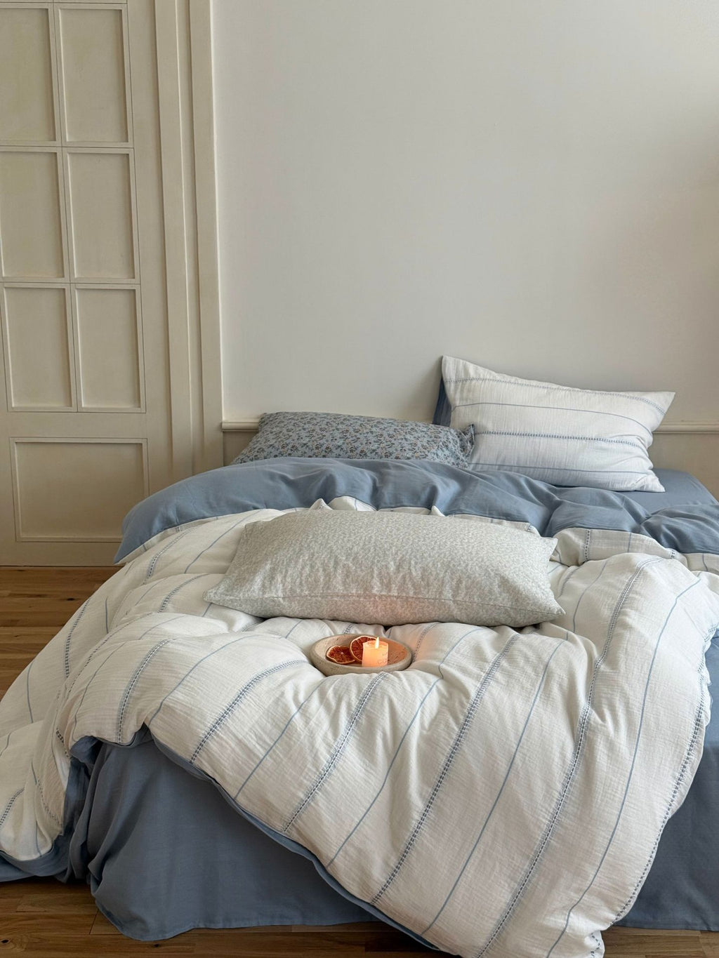 Bed with blue and white bedding, candles, and pillows in a room.