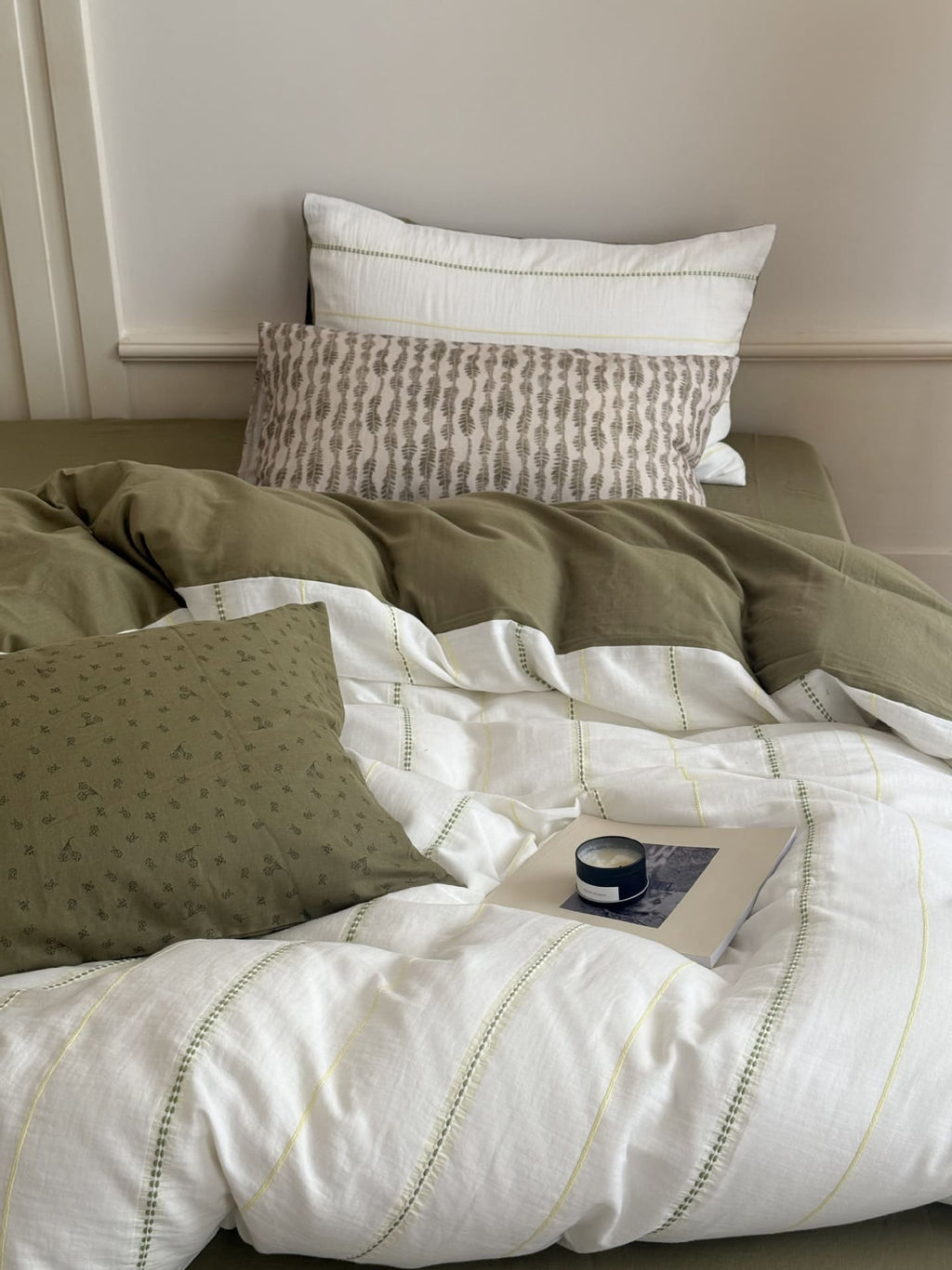 Bed with green and white bedding, pillows, and a small table with a cup.