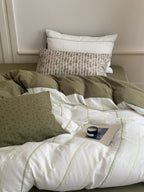 Bed with green and white bedding, pillows, and a small table with a cup.