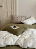 Bed with green and white bedding, pillows, and a small tray with items on a neutral-colored wall.
