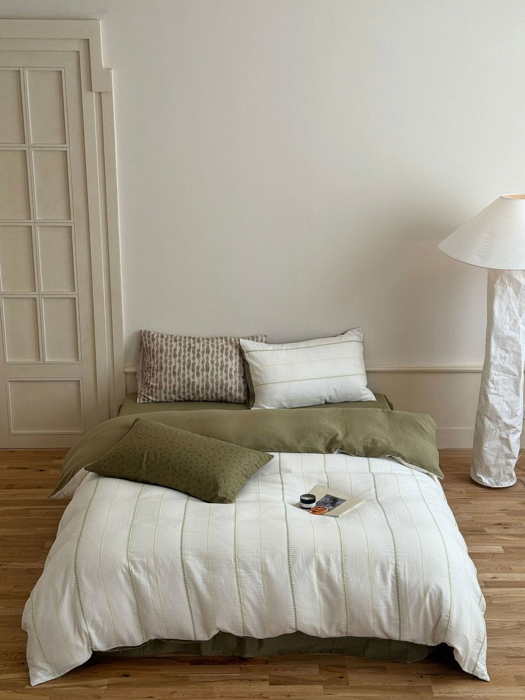 Bedroom with a bed featuring green and white bedding, a lamp, and a wooden floor.