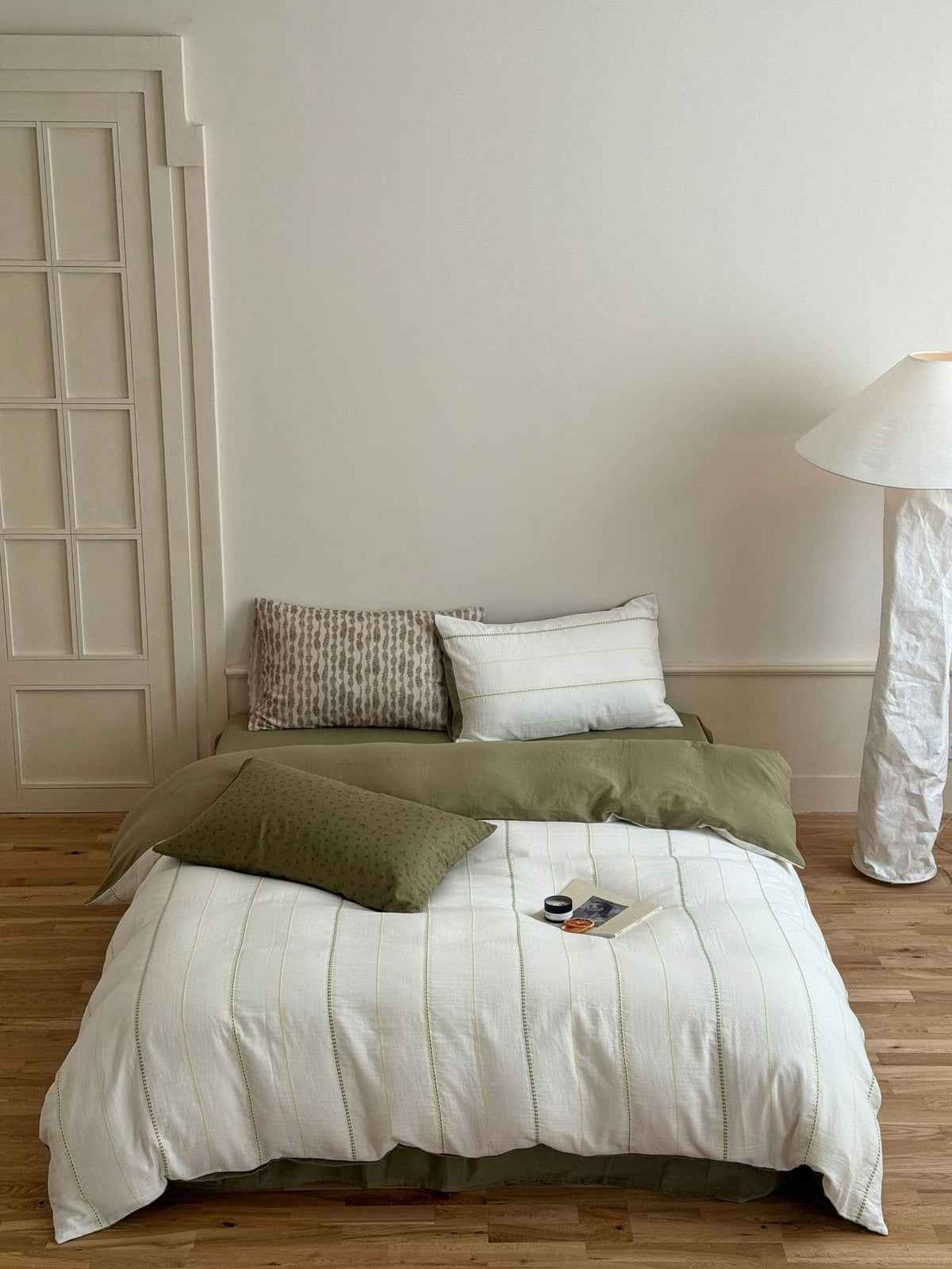 Bedroom with a bed featuring green and white bedding, a lamp, and a wooden floor.