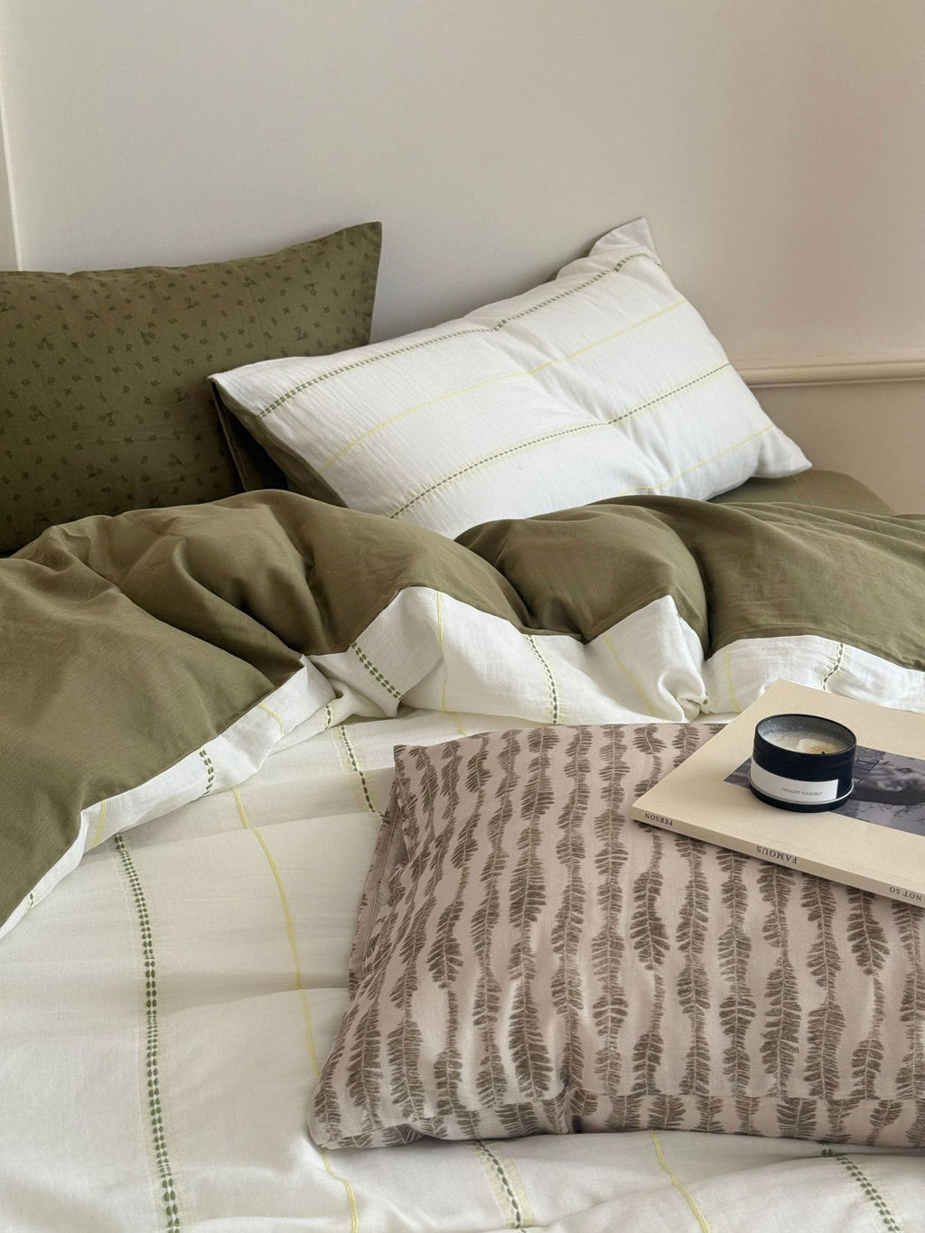 Bed with olive green and white bedding, including a patterned pillow and a small tray.