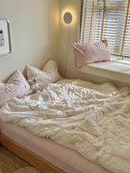 Bedroom with a bed featuring white bedding and pink pillows, illuminated by natural light.